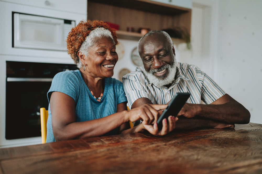 older Black couple smiling looking at a phone
