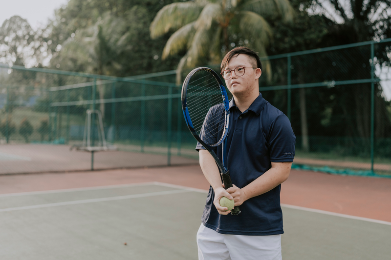 young asian man with down syndrome playing tennis at a local court