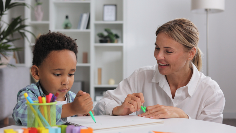 blonde woman draws with marker with a young boy with intellectual disability