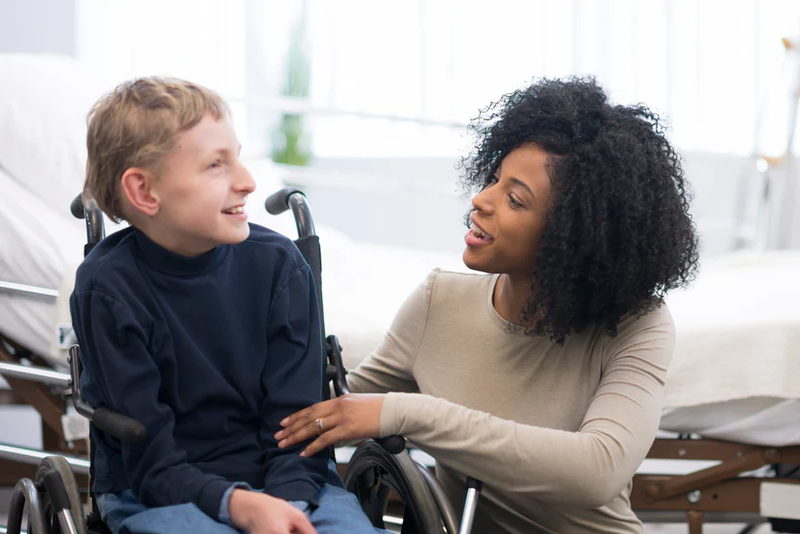 occupational therapist helping a young boy with a disability in a wheelchair