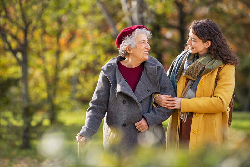 young woman holding an older woman's arm while the two walk together in the fall