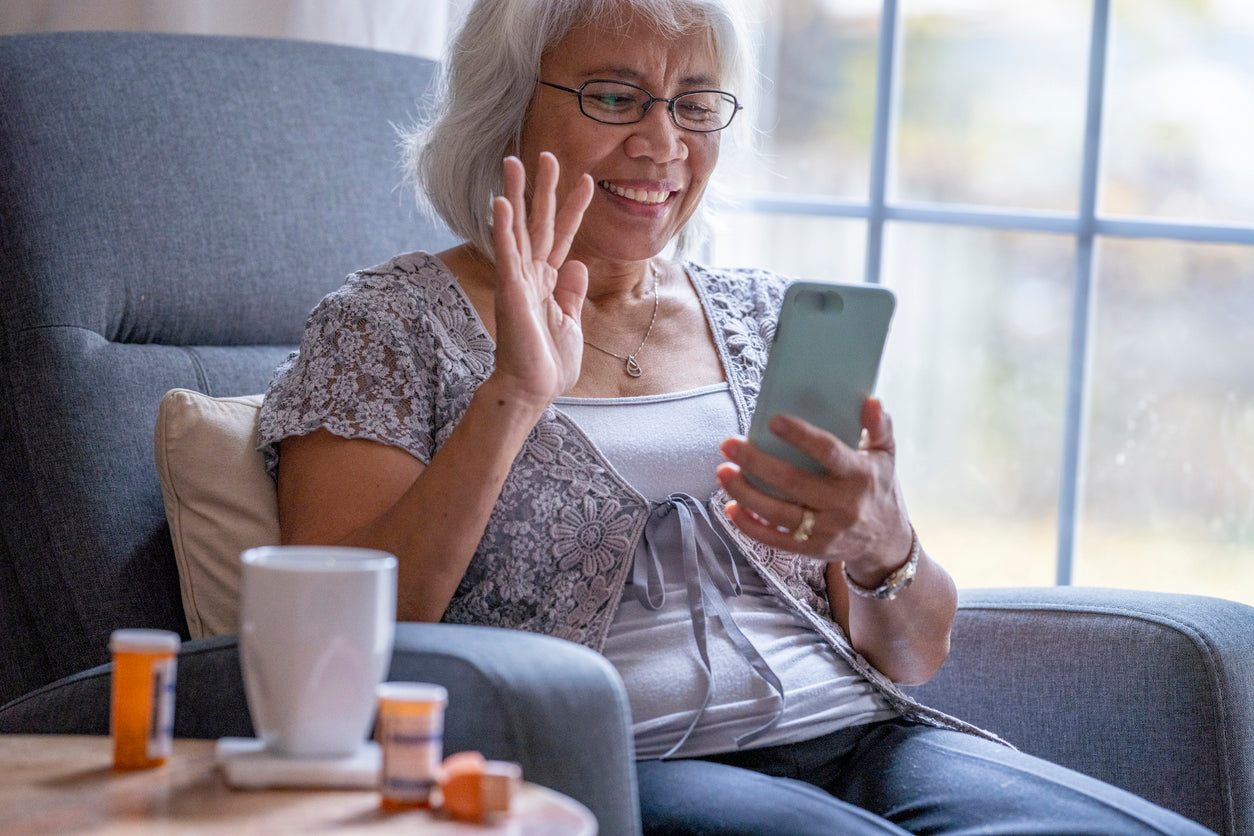 older woman sitting in chair on video call with medication beside her